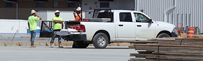 three construction workers talking around white truck with MOLLE panel and toolbox. 